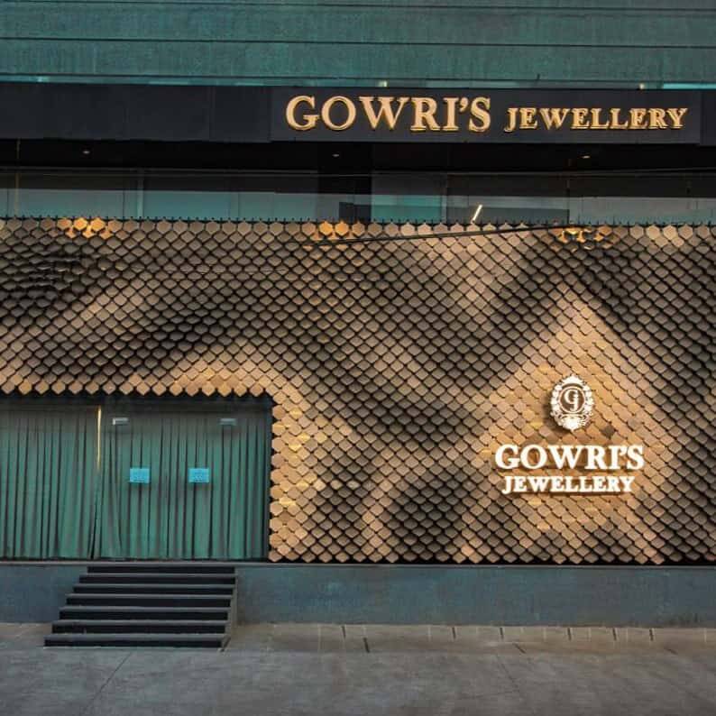 Facade Works Package Scope Split for Builders 2026 4 Bronze overlapping metal scale skin covering a ground-floor showroom elevation seen straight on at street level