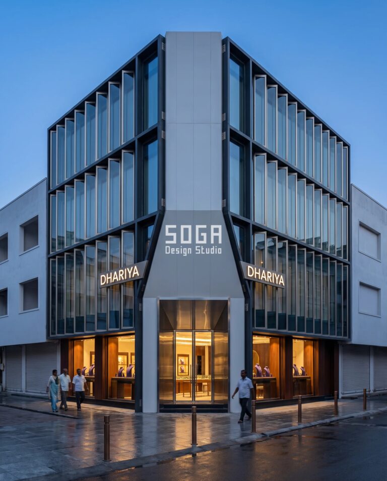 Chamfered corner jewellery showroom facade in Vijayawada, the 45-degree cut face carrying the entrance between two pleated low-iron glass street elevations at dusk
