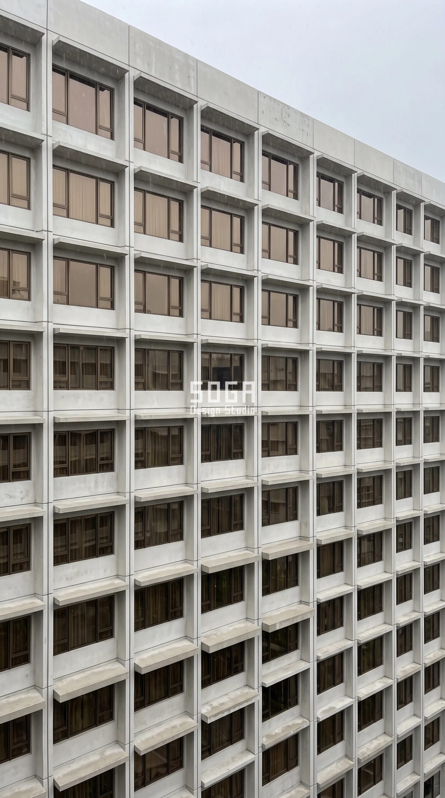 Parametric Brim Course Unit commercial facade in Singapore - acid-etched pale oyster-grey UHPC units on a G+10 business hotel in tropical rain, constant 380 mm brim with front-edge thickness stepping 40 to 140 mm - SOGA Design Studio