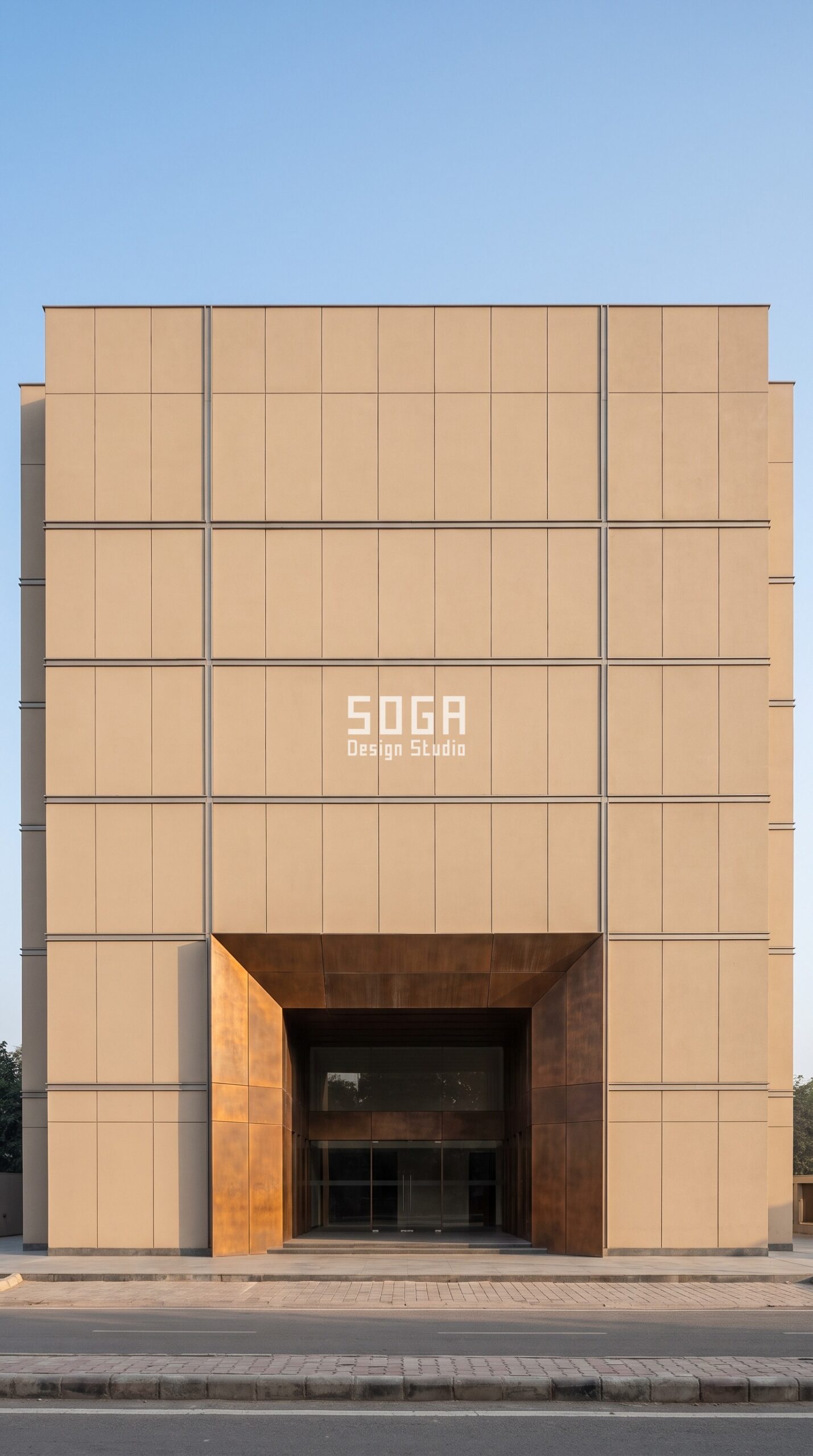 Why Facade Design Matters for Commercial Buildings 2026 4 Commercial building facade with tall recessed bronze entrance bay in a calm panel field, New Delhi India - SOGA Design Studio