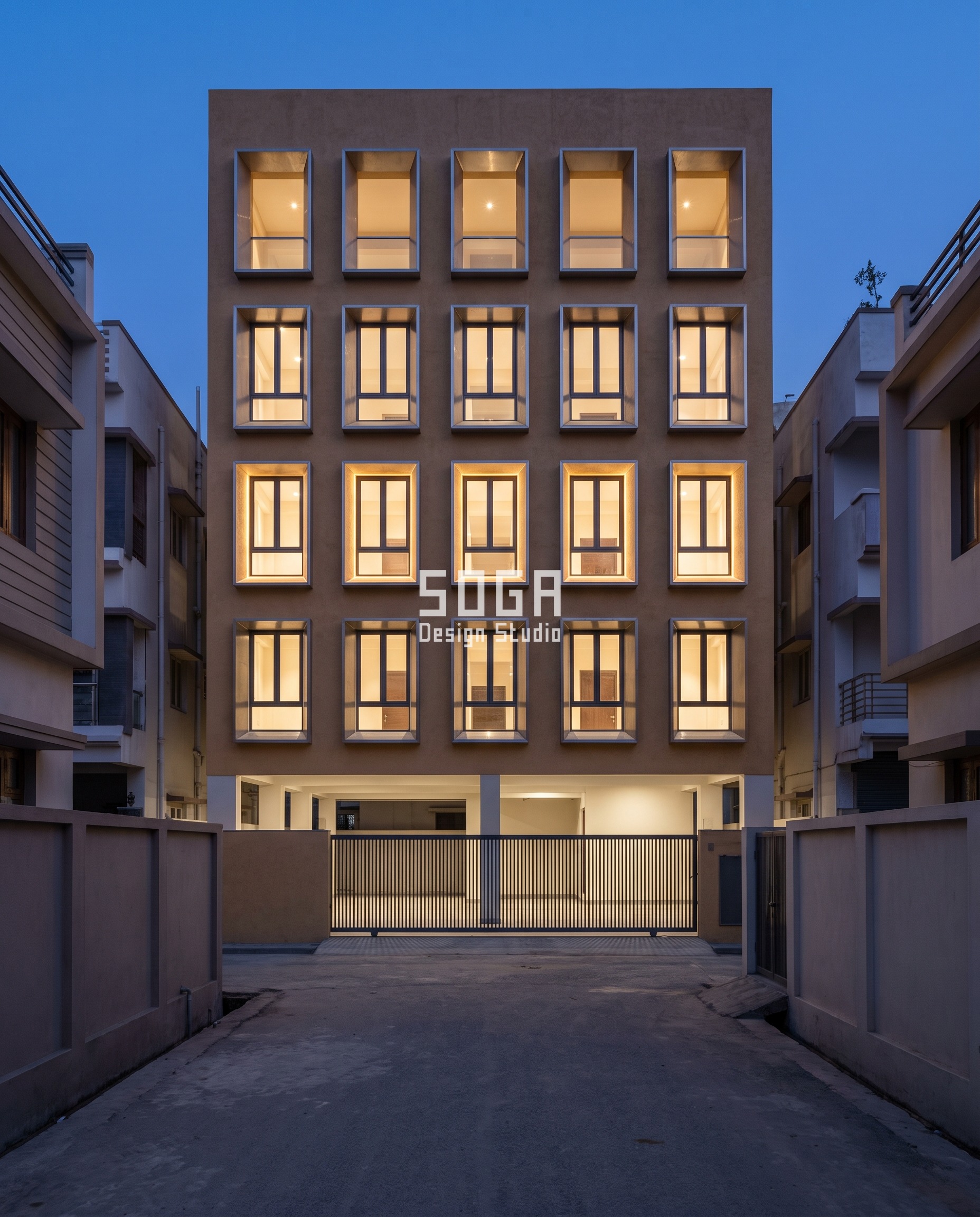 Parametric Jamb Well residence in Tilkamanjhi, Bhagalpur at blue hour: sand-ochre render with stainless-lined window wells cutting from flush at the first floor to 600 mm deep at the top, a warm cove light glowing inside every reveal - an elevation changed after slab cast that adds almost no load.
