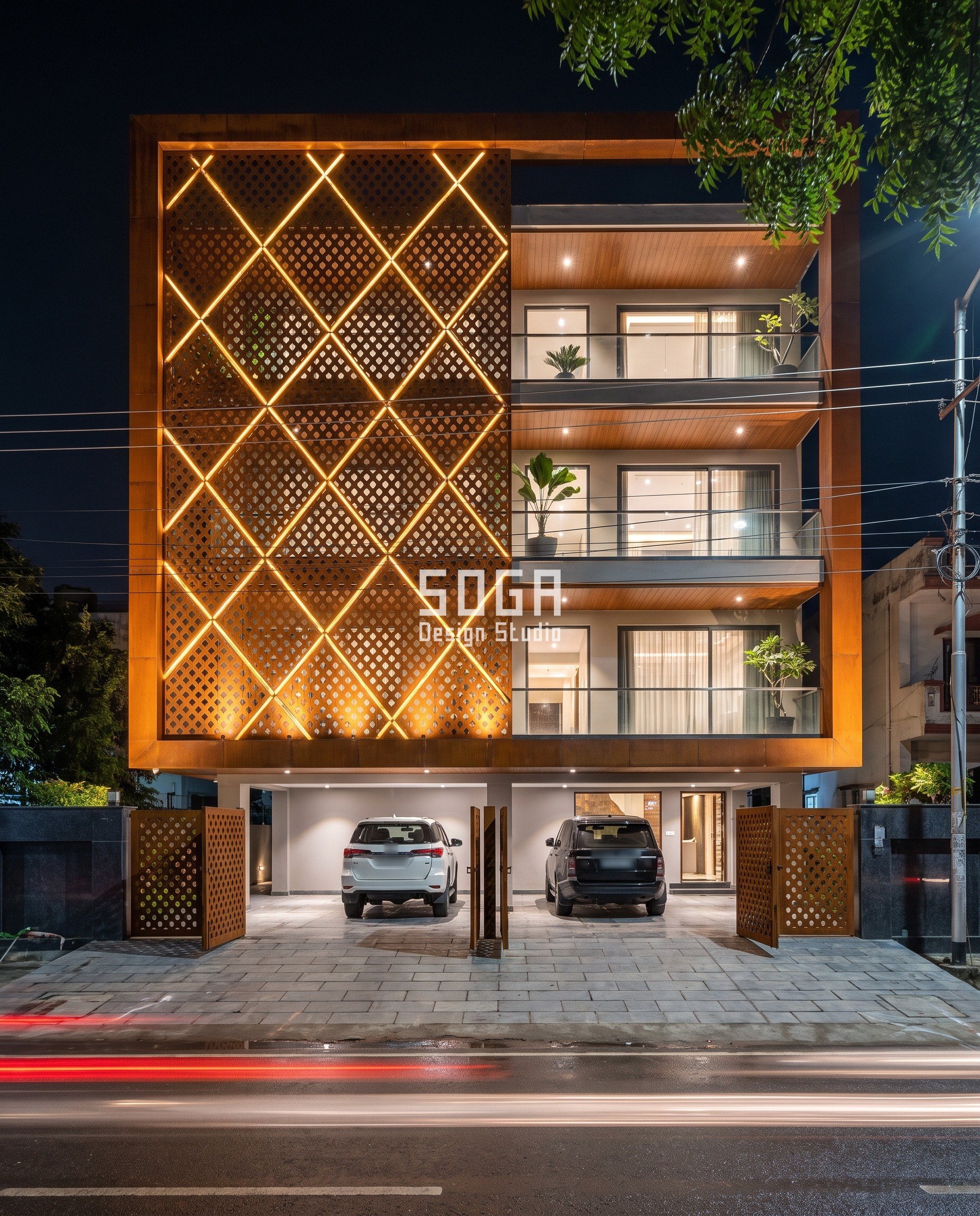 Indo Contemporary Elevation Design: Build for the Street 2 Lucknow house front at night: a deep corten frame holds a diamond jaali lit at every joint over the bedroom half, with clear glass balconies over the living half and matching corten jaali gates at the stilt.