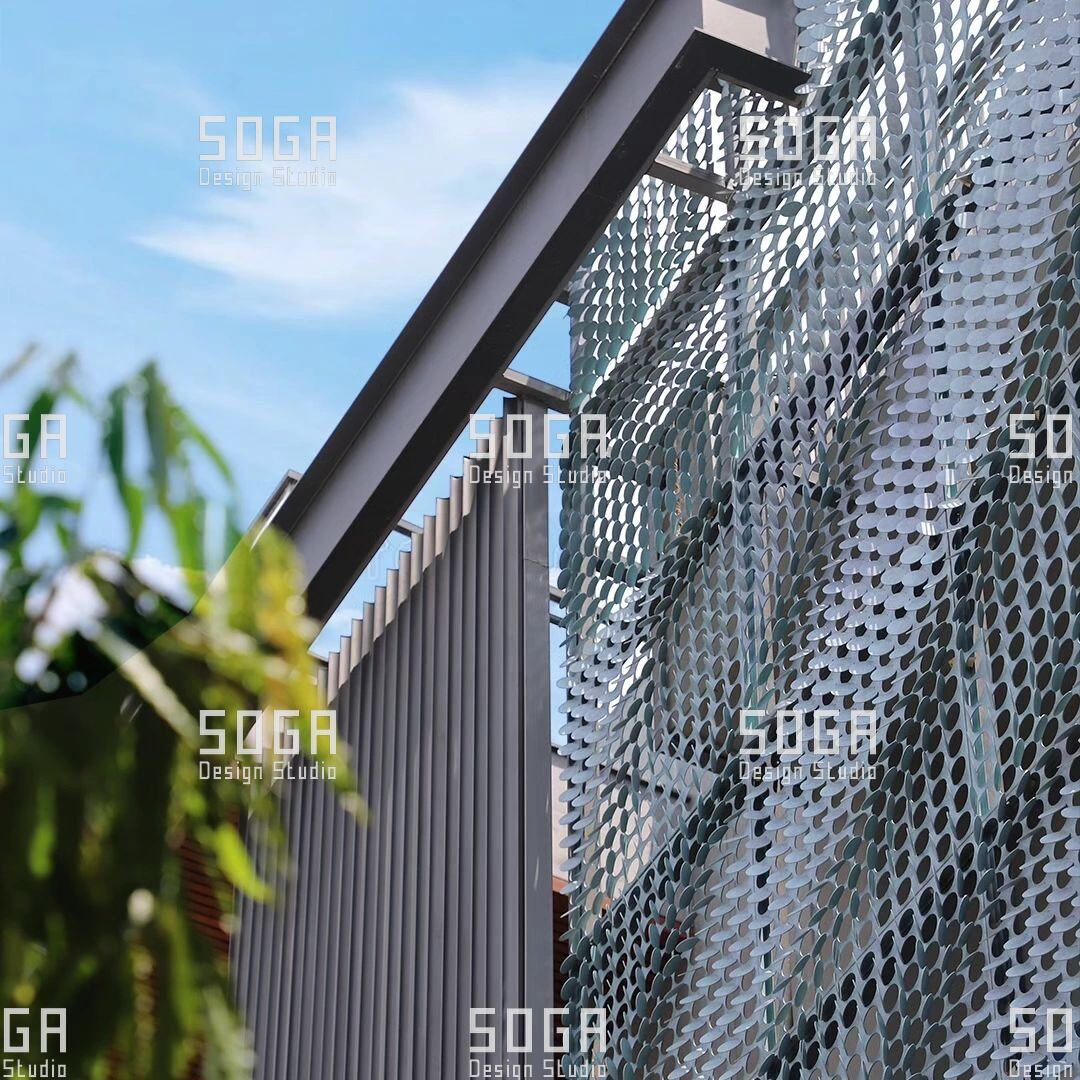 Metal Coin Cladding: Which Buildings It Suits, and Which It Does Not 5 Metal disc screen in front of a residential balcony with planting, giving privacy without closing the opening