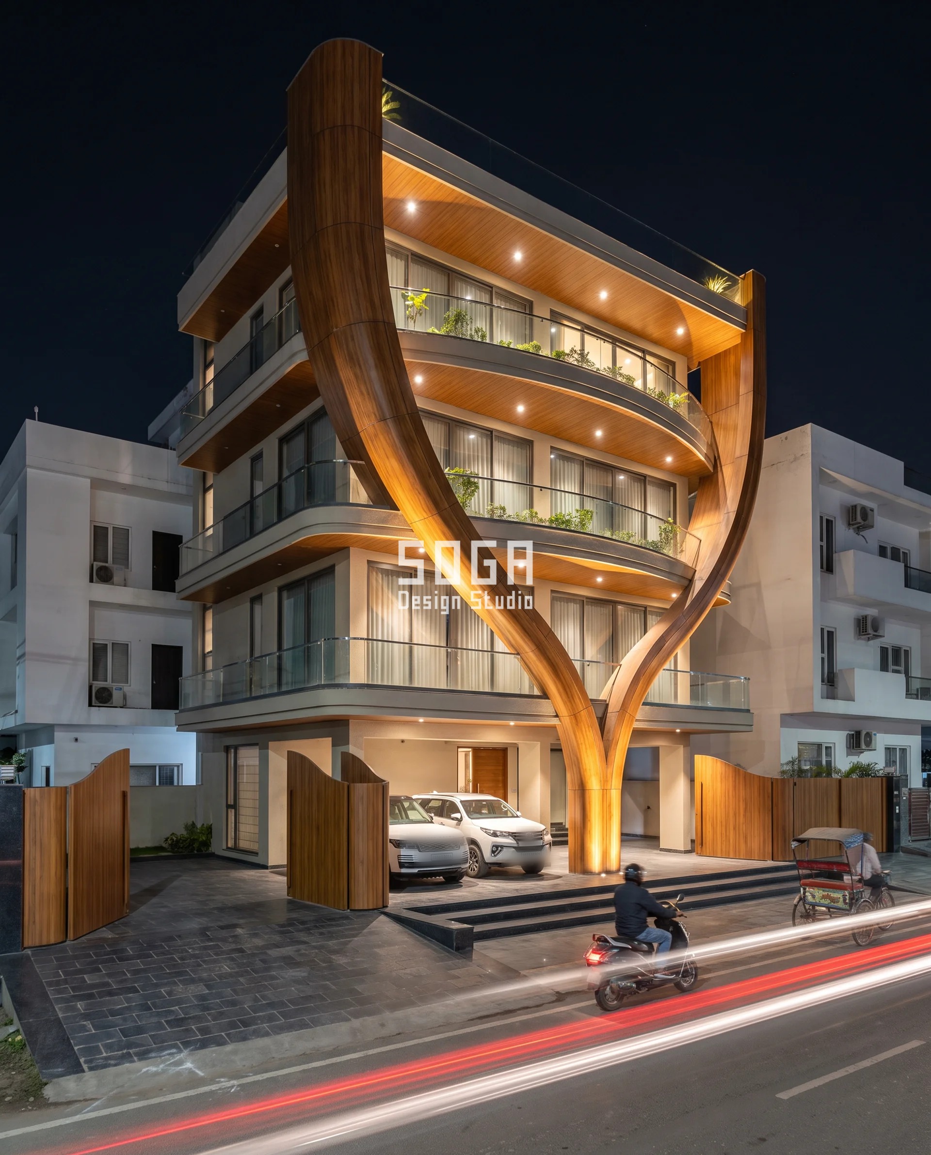 Chandigarh builder-floor facade, Mudra Niwas, where a single teak wood-finish metal frame grows from one slender root at the stilt parking and splits into two leaf-like arms that climb past the parapet, framing curved glass balconies at each floor